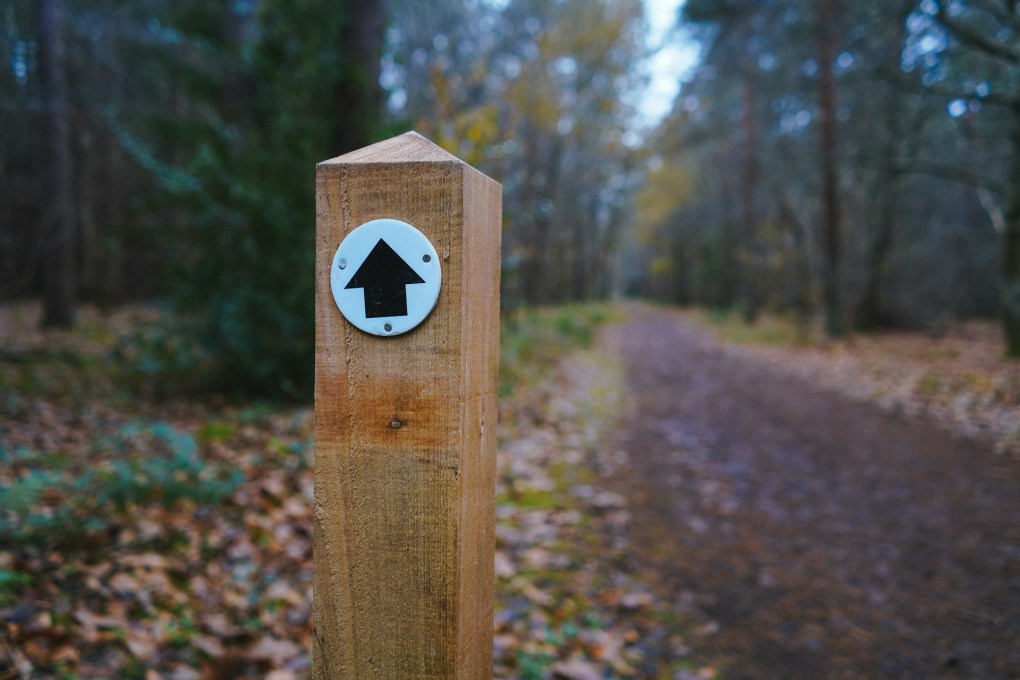 Brown wooden cross with white arrow sign.