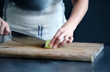 person slicing green vegetable on chopping board